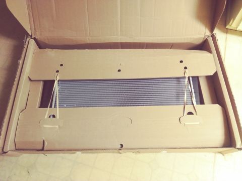 1996 Ford Bronco - A new radiator is shown inside its cardboard packaging, secured with elastic straps. The radiator is a rectangular metal component with a g…