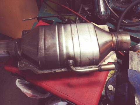 1996 Ford Bronco - A close-up, overhead view of a catalytic converter with inlet and outlet pipes, mounted on a red surface with various tools and equipment i…