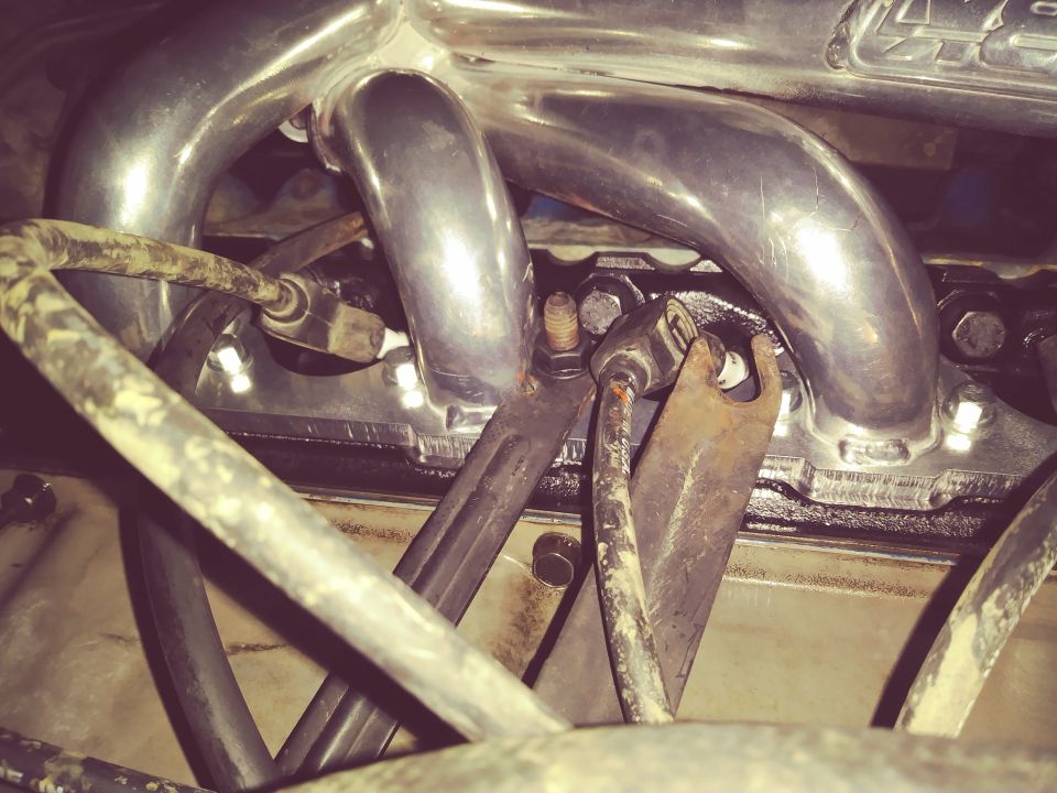 Polished exhaust headers on an engine block with hoses and brackets.