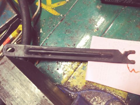 1996 Ford Bronco - A close-up, angled view of a black metal bracket with a C-shaped notch at one end and an oval hole at the other, resting on a pink piece of…