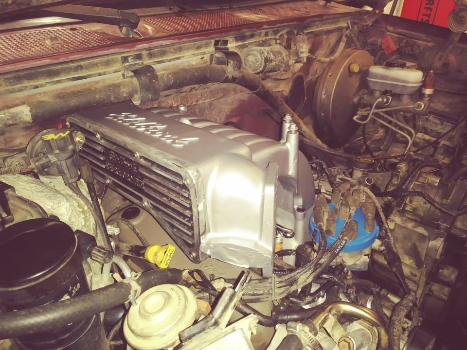 Engine bay of a red Ford Bronco with a silver Edelbrock intake manifold.