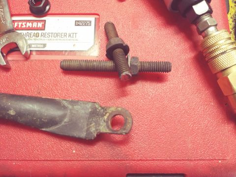 1996 Ford Bronco - A close-up shot shows a Craftsman thread restorer kit, a bolt with nuts and washers, and a metal bracket on a red textured surface.