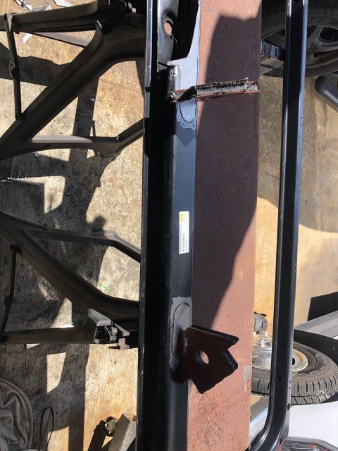 1992 Jeep Wrangler - A black metal frame part with a rusted metal panel behind it is shown outdoors. The frame has a small white sticker with black text.