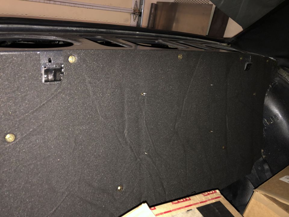 Black sound-deadening material covering the rear interior of a vehicle, secured by screws and mounting brackets.