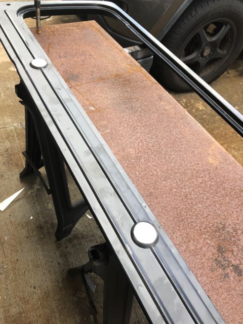 1992 Jeep Wrangler - A black metal trim piece with two white circular inserts is resting on a rusty metal surface supported by black sawhorses. A portion of a d…