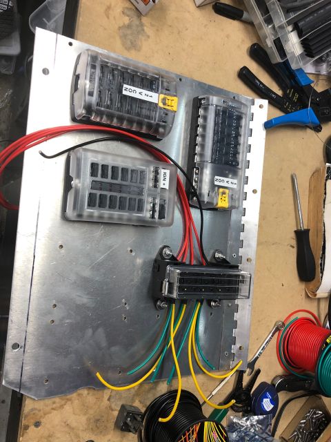 1992 Jeep Wrangler - A metal panel with multiple fuse blocks and wiring is mounted on a workbench. Red, black, yellow, and green wires are connected to the fuse…