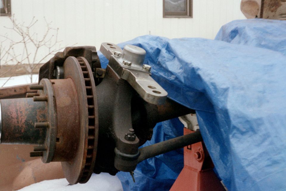 Close-up of rusty brake rotor and steering linkage components, partially covered by a blue tarp