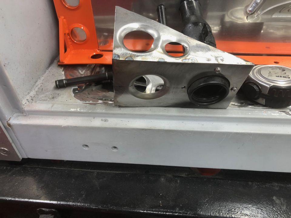 Custom metal bracket with holes and a rubber grommet on a vehicle floor.