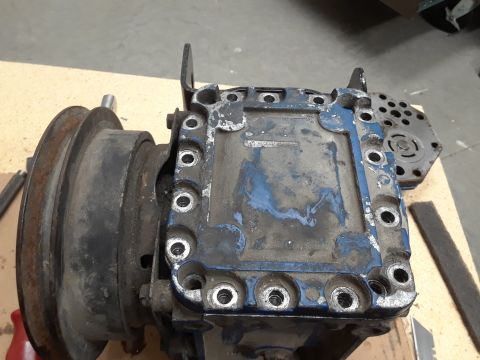 1985 Ford Bronco - A close-up view of a disassembled hydraulic motor or pump assembly, featuring a large pulley on the left and a blue-coated housing with num…