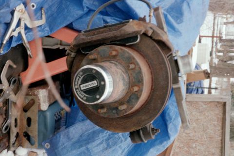 1979 Ford Bronco - Close-up of a rusty vehicle hub assembly, a WARN locking mechanism and brake rotor, partially covered by a blue tarp.