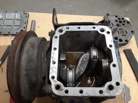 1985 Ford Bronco - A disassembled engine component with internal crankshaft and connecting rods submerged in oil. A metal cover with a grid pattern and a circ…