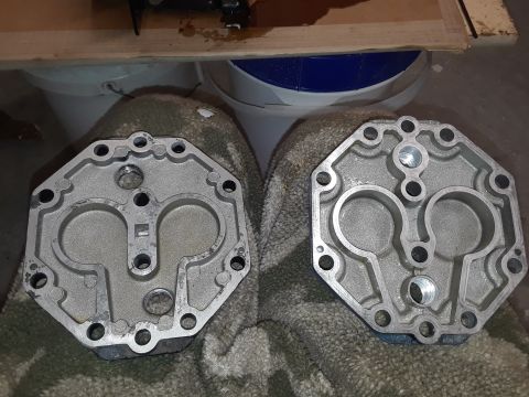 1985 Ford Bronco - Two aluminum engine parts, likely cylinder heads or similar components, are laid out on a textured cloth. The parts have a complex internal…