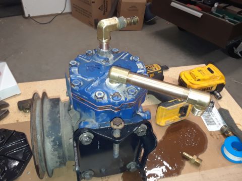 1985 Ford Bronco - A blue air conditioning compressor is mounted on a black bracket, with brass fittings and tubing attached to the top and side. Tools and a…