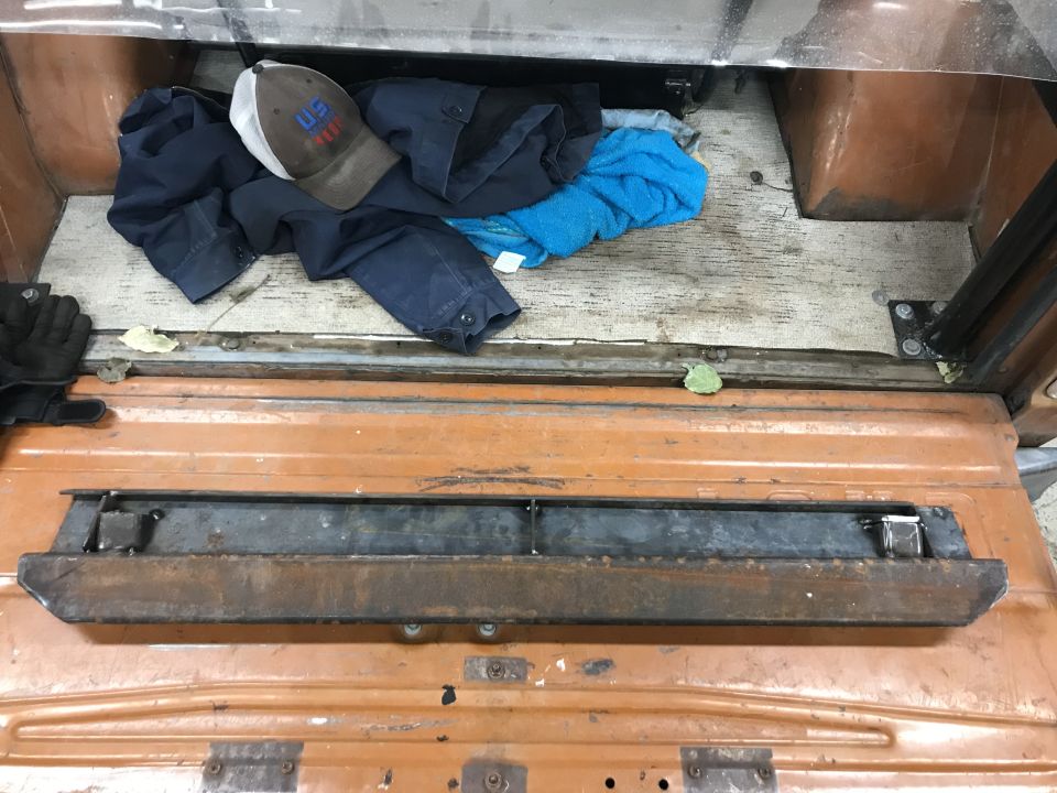 Rear interior of a vehicle with clothes and a hat, and a rusty metal bracket on the exterior.