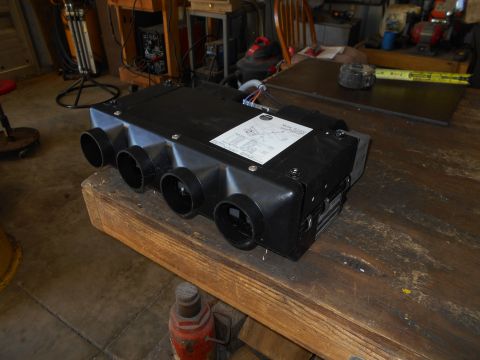 1992 Ford Bronco - A black HVAC unit with multiple circular vents sits on a wooden workbench. A label with text and diagrams is affixed to the top of the unit.