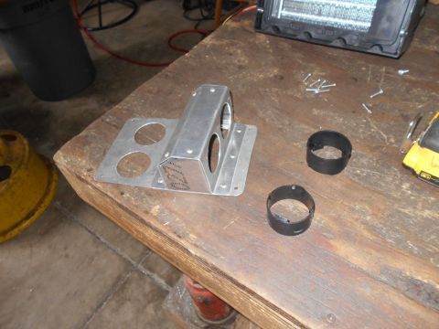 1992 Ford Bronco - A metal bracket with circular cutouts sits on a wooden workbench next to two black rings and some screws. A yellow object and a black trash…