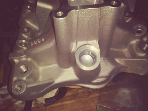 1996 Ford Bronco - A close-up, angled view of a silver-colored metal automotive part, possibly an intake manifold, with visible casting marks and a threaded h…