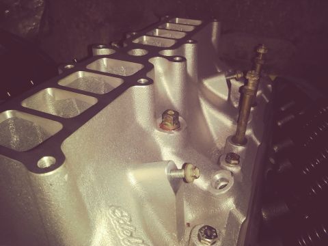 1996 Ford Bronco - A close-up, angled view of a silver aluminum intake manifold with multiple intake ports. Several bolts and a brass fitting are visible on t…