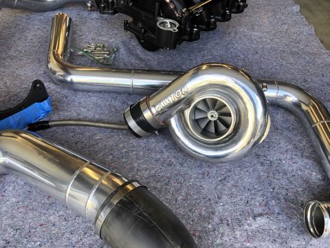 1998 Ford Crown Victoria - Engine parts, including a Paxton supercharger and polished intake pipes, are laid out on a gray surface.