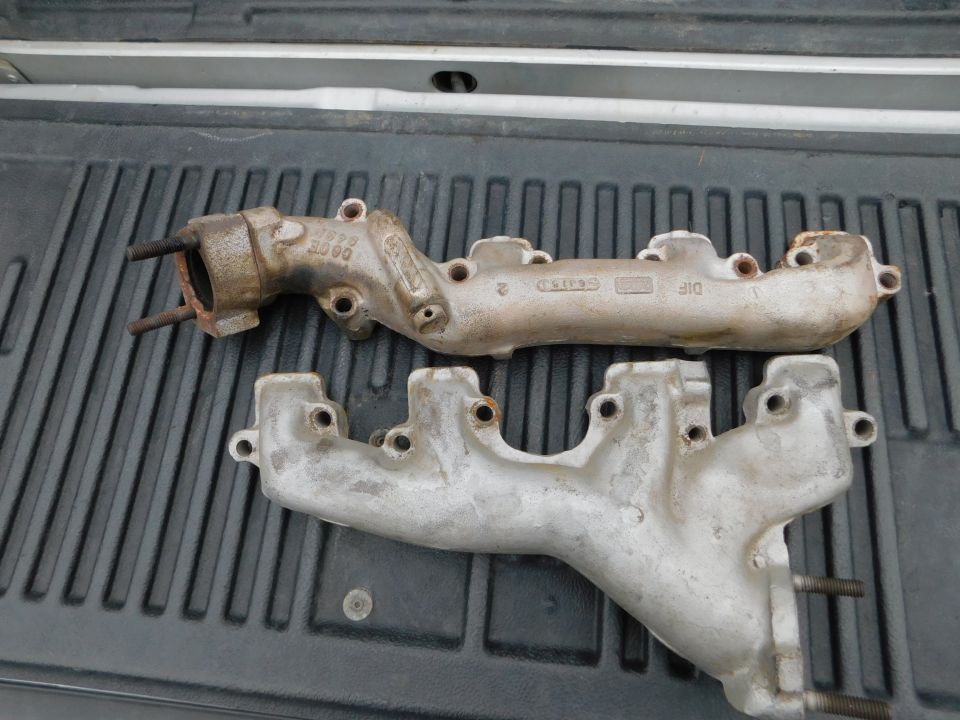 Two rusty cast iron exhaust manifolds in a truck bed liner