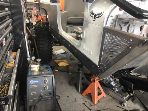 1992 Jeep Wrangler - A Jeep Wrangler body is elevated on jack stands in a workshop, with a Miller welding machine nearby.