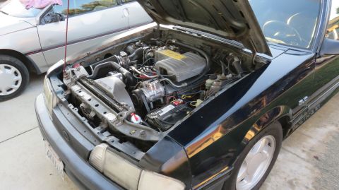 1988 Ford Mustang - Engine bay of a black 1988 Ford Mustang, with another vehicle partially visible.