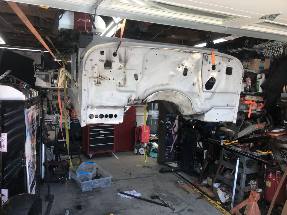 Jeep CJ/YJ body shell, stripped down and suspended by straps in a cluttered garage