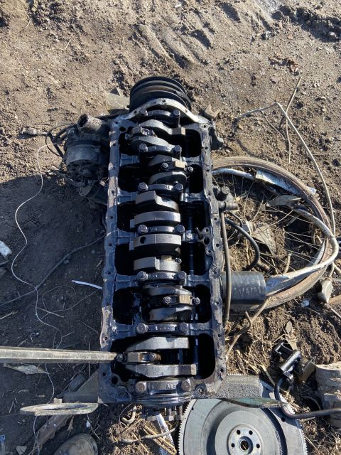 1994 Ford Bronco - An engine block with its crankshaft exposed sits on the dirt, with a bicycle wheel visible in the background.