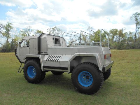1992 Ford Bronco - This custom-built vehicle features a unique, utilitarian design with large off-road tires and bright blue wheel rims.