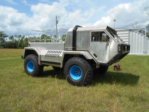 1992 Ford Bronco - A unique, heavily modified vehicle with a metallic finish and bright blue wheels sits in a grassy outdoor area.