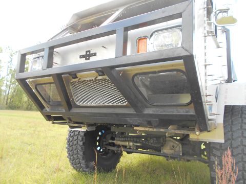 1992 Ford Bronco - The front of a heavily modified vehicle with a custom bumper and off-road tires is shown in a grassy field.