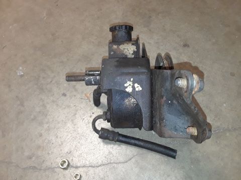 1994 Ford Bronco - A detached black power steering pump assembly rests on a concrete surface.