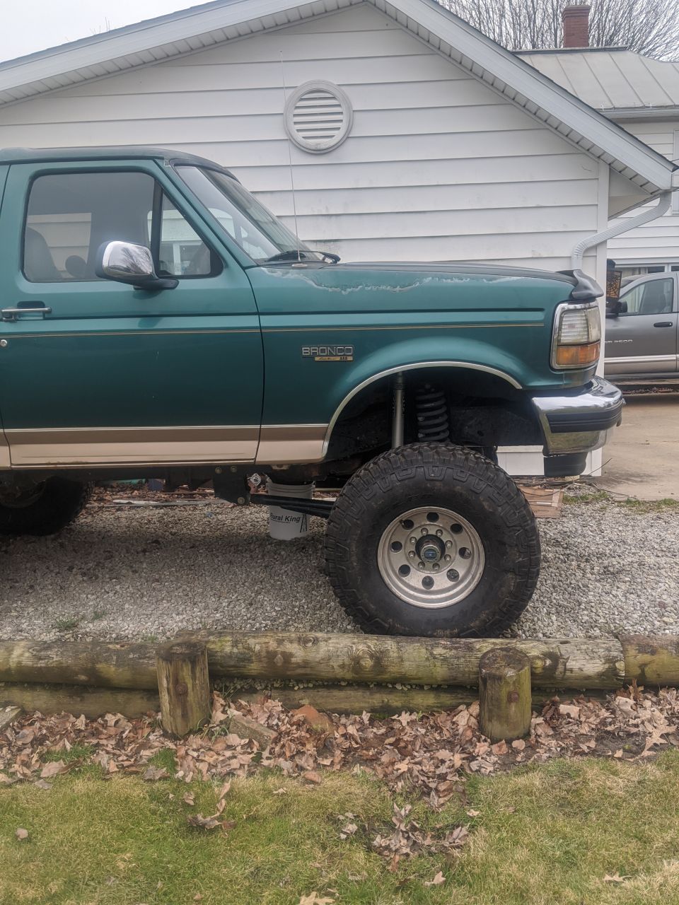 Green Ford Bronco with lifted suspension and large tires parked outside a house