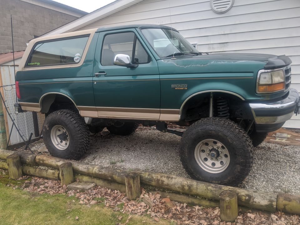 Green 1996 Ford Bronco with tan top, lifted suspension, and large tires parked on gravel