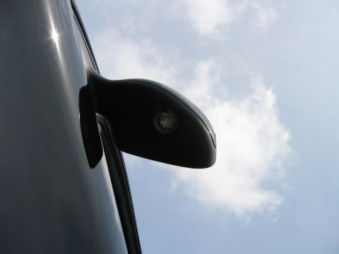 2002 Ford Taurus - A close-up shot of a vehicle's side mirror and adjacent body panel, set against a backdrop of clouds and blue sky.