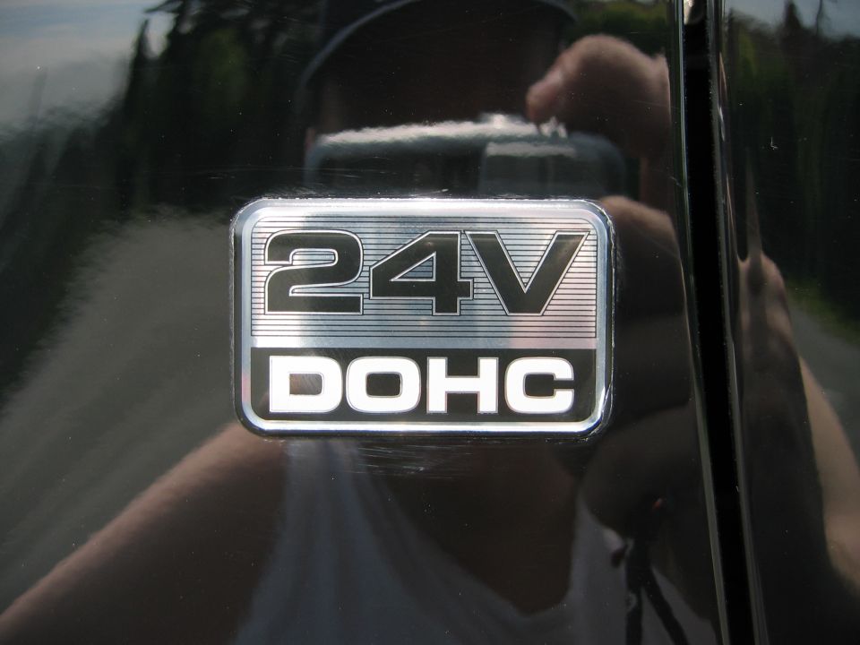 Black car fender with a silver 24V DOHC badge, showing scratches and reflections