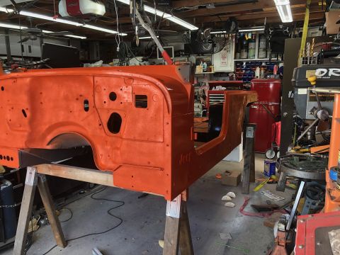 1992 Jeep Wrangler - The body of a Jeep is shown in an orange primer color, resting on sawhorses in a workshop.
