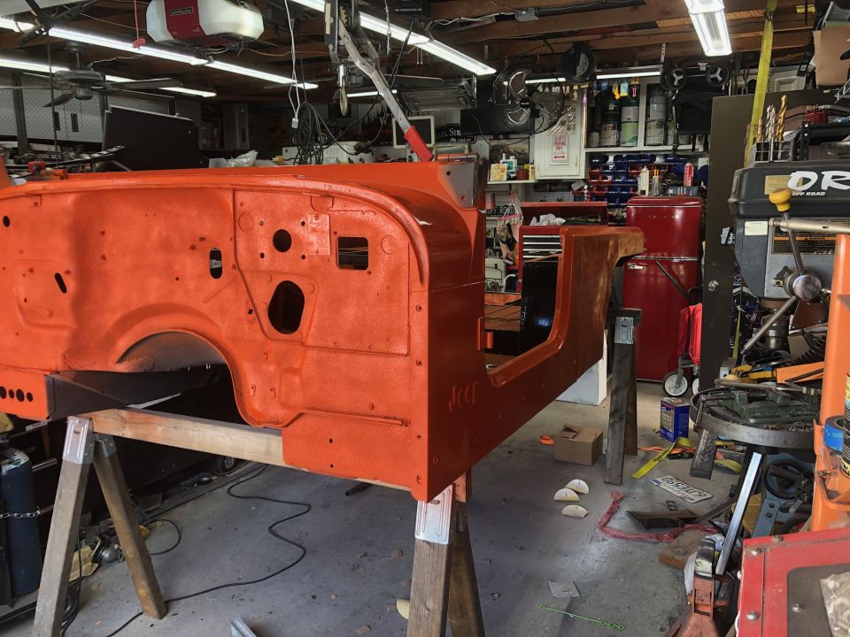 Orange Jeep tub on sawhorses in a garage, undergoing restoration