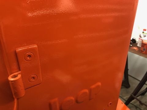 1992 Jeep Wrangler - Glossy orange-painted body panel with embossed 'Jeep' lettering and a painted door hinge in a garage.