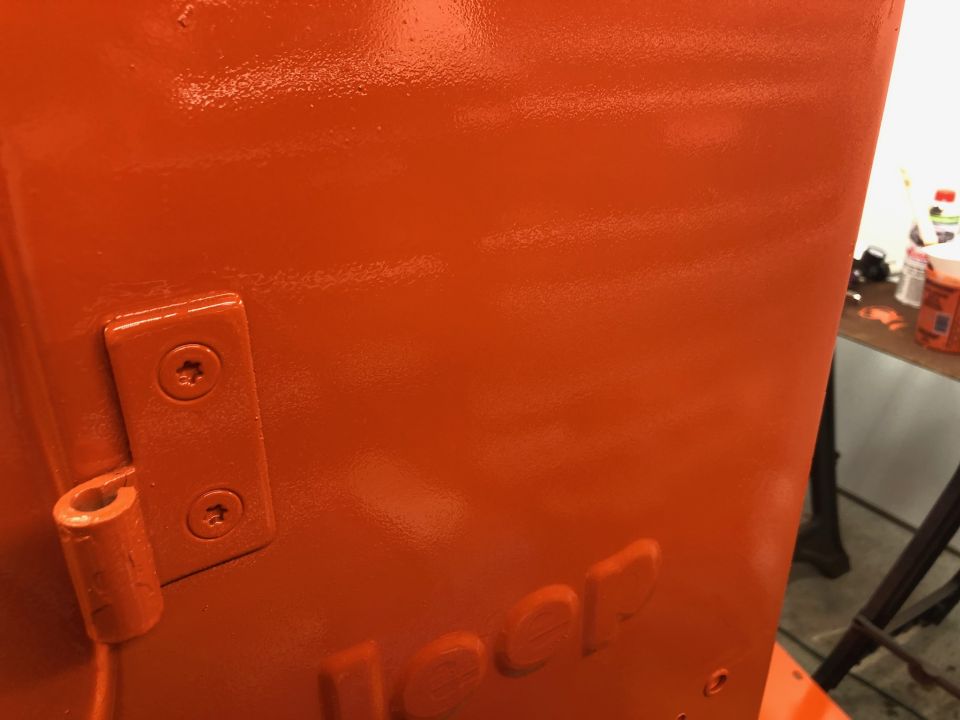 Freshly painted orange Jeep body panel with embossed Jeep logo and hinge