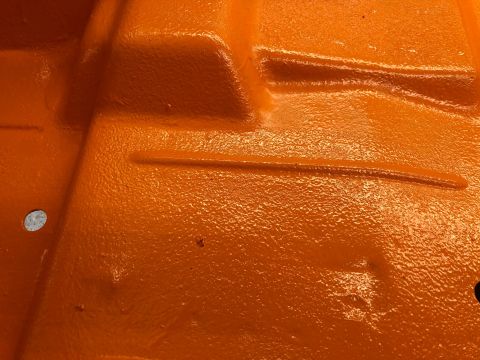1992 Jeep Wrangler - Close-up of an orange painted metal floor pan, showing its textured surface and structural details.