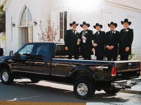 2002 Ford Taurus - A black pickup truck is parked in front of a white building, with five men dressed in cowboy hats and tuxedos standing in the truck bed.