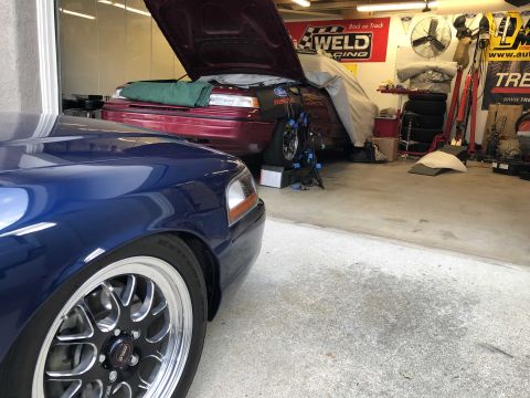 1992 Ford Crown Victoria - A dark blue car is parked in the foreground of a garage, with a red car partially covered in the background.