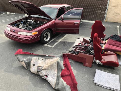 1992 Ford Crown Victoria - A maroon 1992 Ford Crown Victoria is shown with its hood and doors open, revealing its engine and disassembled interior components.
