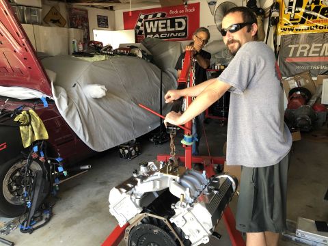 1992 Ford Crown Victoria - Mechanics work on an engine being removed from a car in a garage setting.