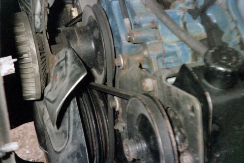 1979 Ford Bronco - Tight engine-bay shot of the front accessory drive on a blue-painted V8, showing the crank and water pump V-belt pulleys, a steel accessory…