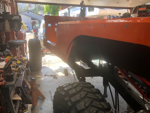 1992 Jeep Wrangler - The orange body of a Jeep CJ-7 is shown in a garage, lifted on jack stands with large tires attached.