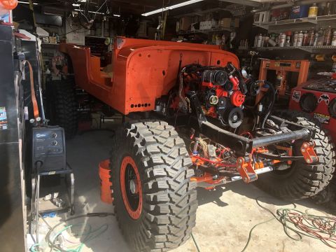 1992 Jeep Wrangler - An orange Jeep Wrangler body and engine are visible in a garage, undergoing modifications with large off-road tires.