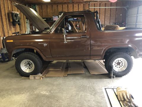 1980 Ford Bronco - A brown 1980 Ford Bronco is parked in a garage with its hood up, showing it is undergoing maintenance.