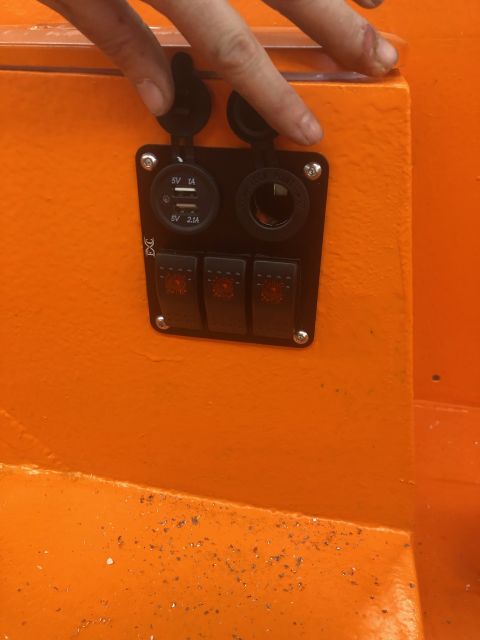 1992 Jeep Wrangler - A hand interacts with a panel of switches and USB ports on an orange surface.